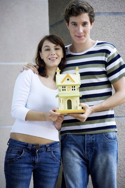 A couple standing in front of a new house, smiling and holding keys. The image suggests they have achieved a significant financial goal together.