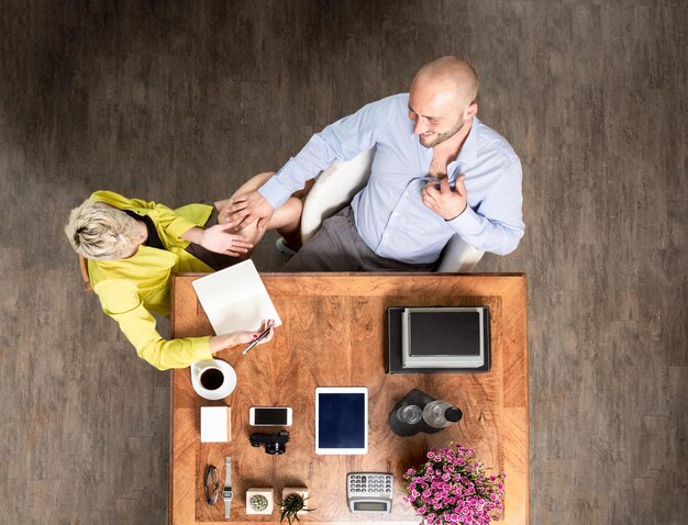 An overhead shot of a couple working together at a desk, using a calculator and a spreadsheet to calculate their proportional contributions, with coffee cups and a plant adding a warm touch to the scene.