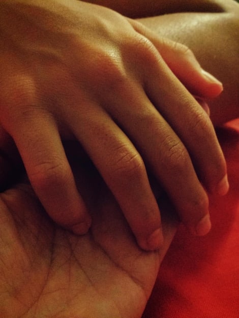 A close-up shot of two hands, one male and one female, clasped together over a pile of money and financial documents on a desk. The focus is on the hands and the money, symbolizing unity and shared financial responsibility.