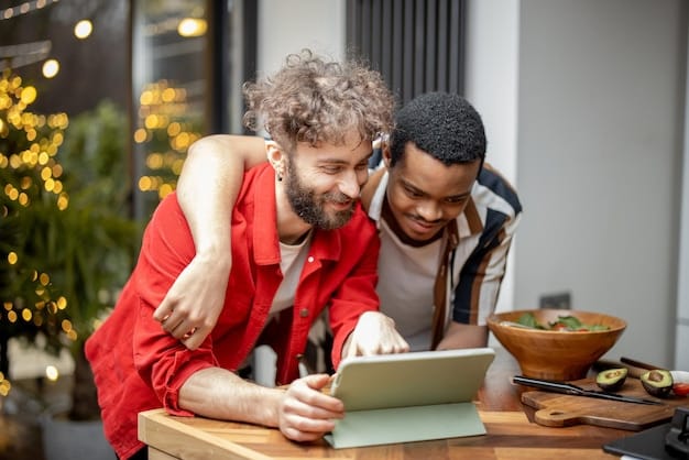 A diverse couple working together on a budget plan in their sunlit kitchen, smiling and pointing at a tablet displaying financial data.