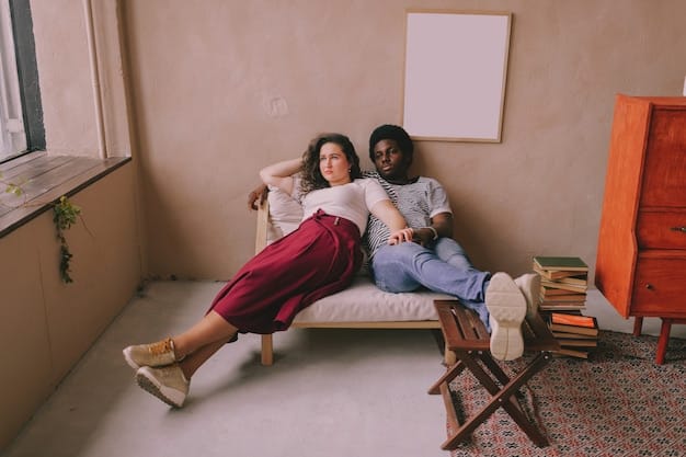 A diverse couple sits comfortably side-by-side on a cozy sofa, smiling and looking at a tablet held by one of them, indicating an engaging and collaborative online therapy session. The background is a soft, inviting home environment.