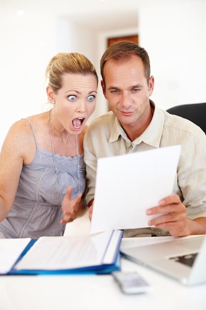 A couple sitting at a desk, looking at a laptop and discussing financial documents with focused expressions.
