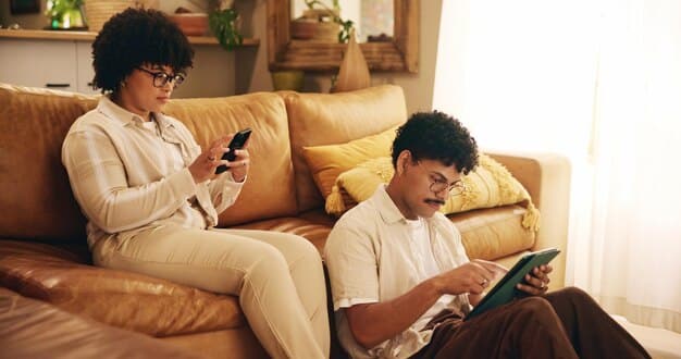 A diverse couple sitting on a sofa, each holding a tablet, looking thoughtfully at the screens. Their expressions are serious yet engaged, indicating deep concentration on financial planning. The background is a cozy, modern living room.