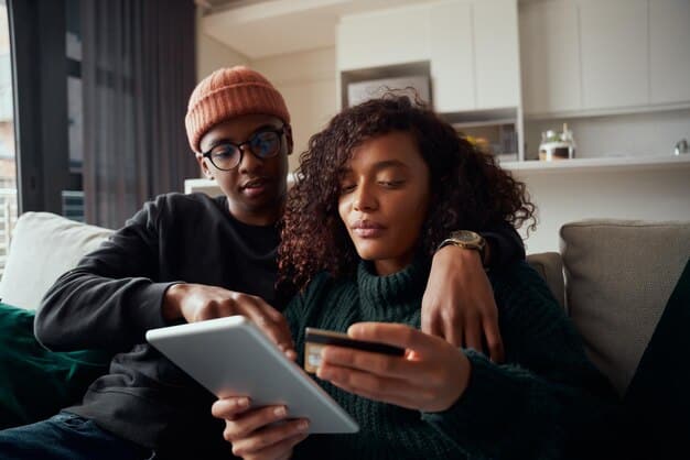 A diverse couple sits on a couch, intently discussing a tablet displaying a financial planner app, highlighting shared decision-making and digital tools in money management.