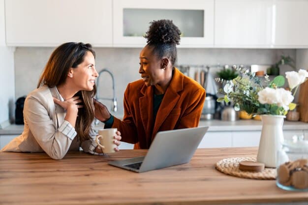 A diverse couple sits at a kitchen table, looking thoughtful while discussing a budget laid out on a tablet, with coffee cups beside them.