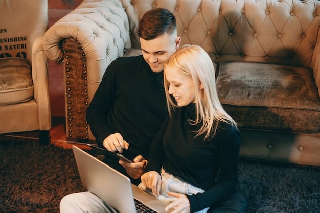 A couple sits on a sofa, looking at a laptop and using a budgeting app. One partner is pointing at the screen, indicating active financial discussion.