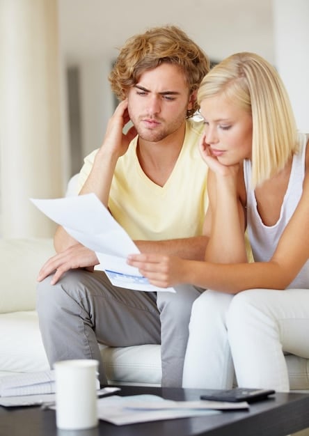 A couple sits at home, looking stressed while reviewing financial statements, highlighting the emotional toll of financial planning, particularly concerning blended family complexities.
