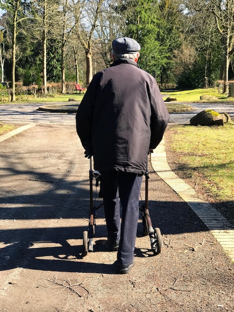 A senior man, using a walker, is carefully walking down a well-lit hospital corridor, demonstrating perseverance and adapted mobility for physical activity.