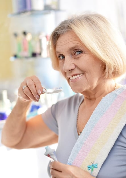 A calm, thoughtful older woman gently flossing her teeth in a well-lit bathroom, demonstrating focused daily oral care.