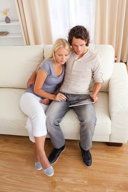 A couple in their 30s or early 40s sitting on a sofa, looking at each other seriously and talking, perhaps with a slight furrow in their brows, illustrating the importance of active listening and open communication in overcoming relationship challenges.