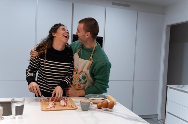 A couple laughing together while cooking in a sunlit kitchen, showing joyful, connected interaction.