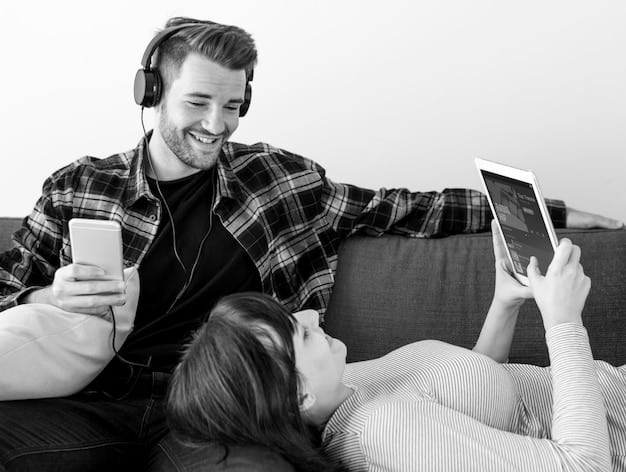 A couple laughing and sharing headphones while sitting close, looking at a tablet together, illustrating healthy shared media consumption and connection.