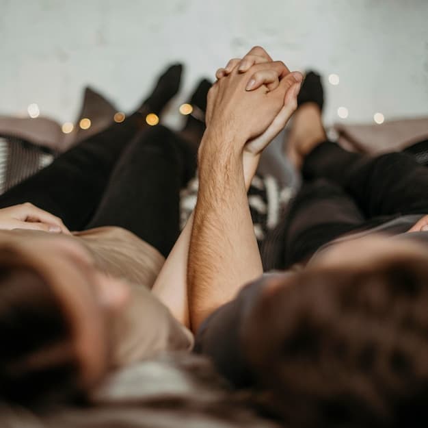 A warm, intimate photo of a couple's hands intertwined under soft lighting, possibly on a bed, conveying comfort and quiet affection.